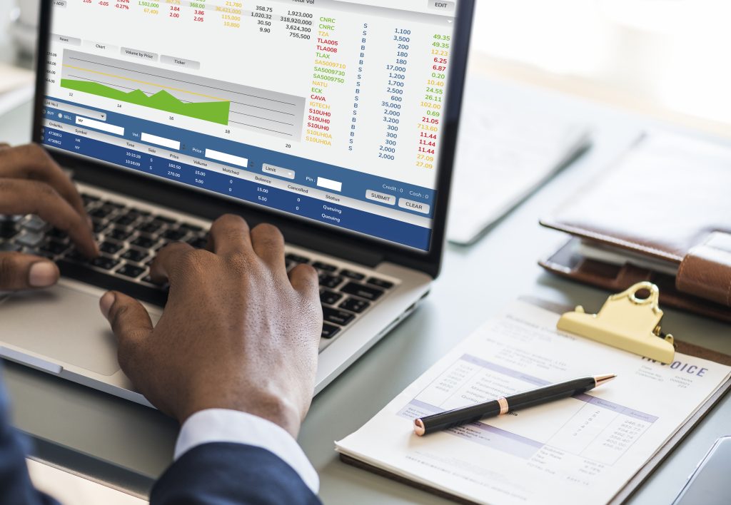 Businessman typing on a laptop that shows charts, next to paperwork