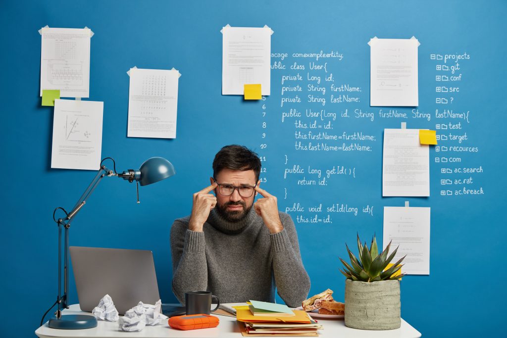 Man in glasses at a desk pressing his temples, looking stressed