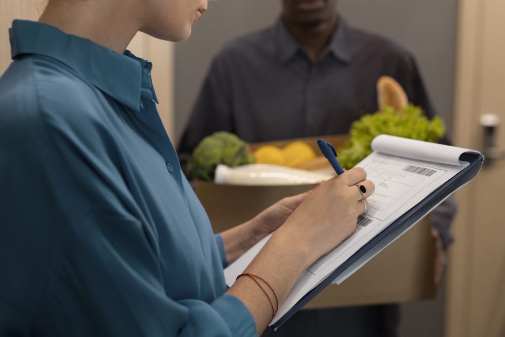 Woman signing a clipboard while receiving a box of groceries