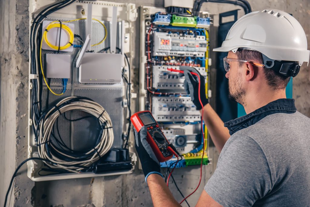 Electrical technician in a hard hat testing a switchboard with a meter